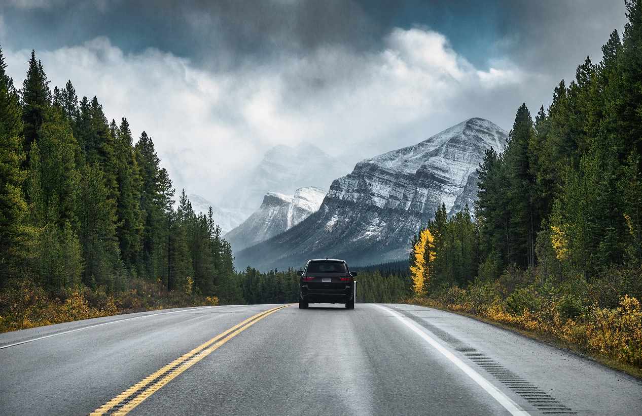 car driving on road in a mountainous landscape with trees lining both sides of the road