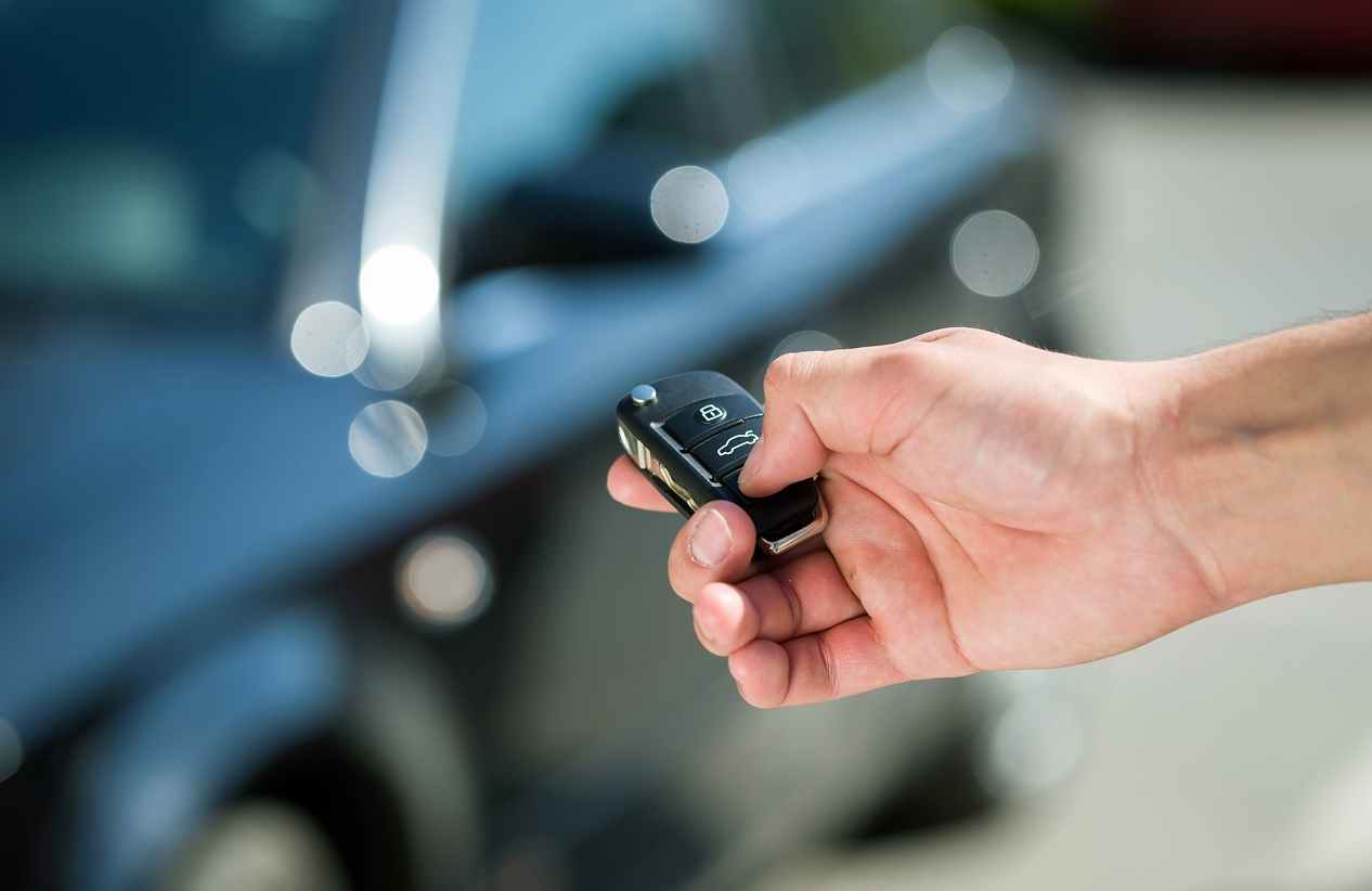 person holding key fob in hand while standing next to car and pressing the unlock button