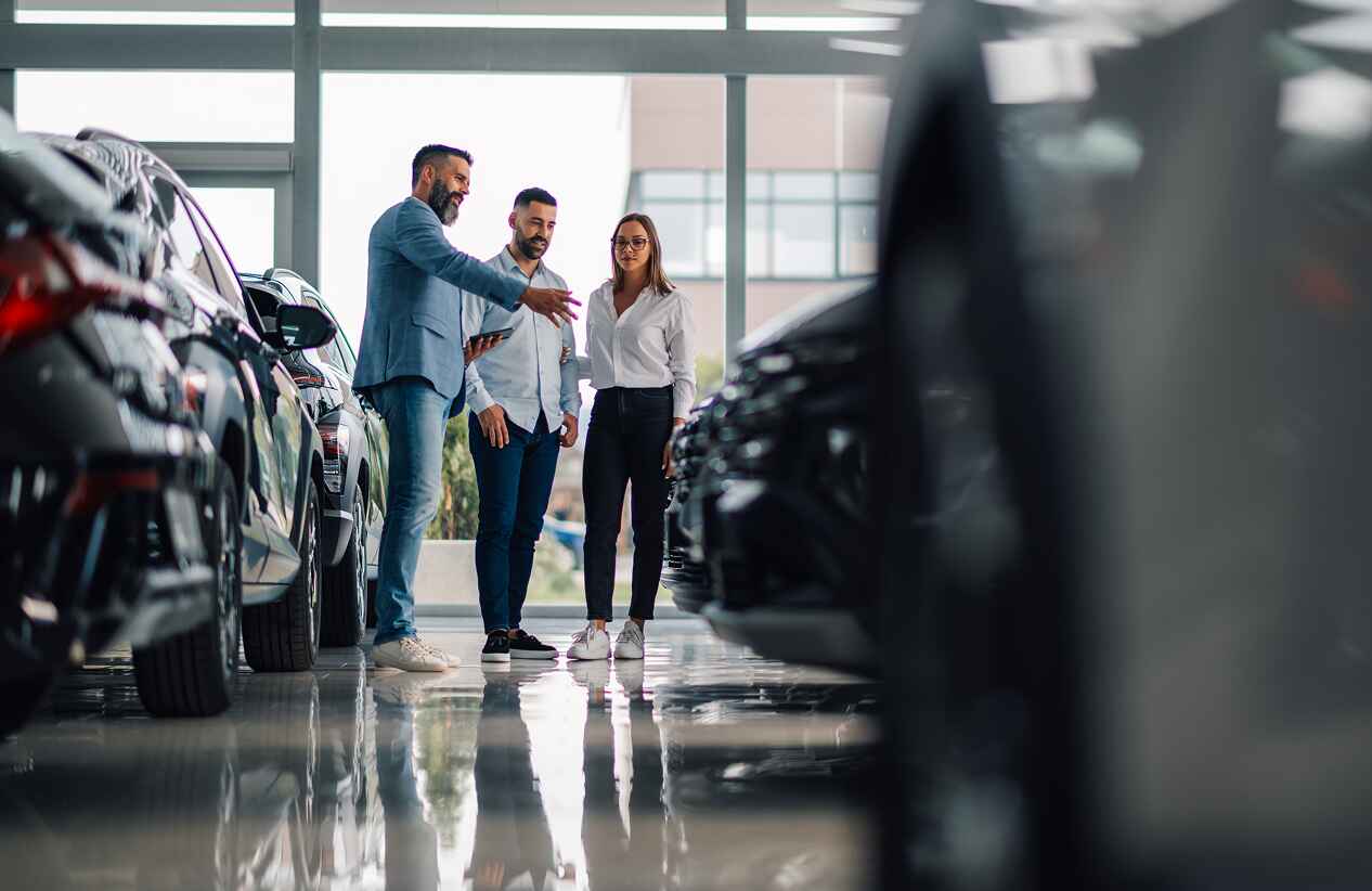 three people standing in a dealership looking at various car models