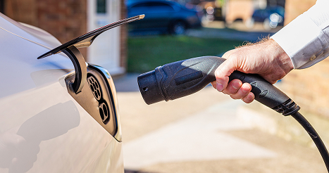 Color image depicting a man charging his electric vehicle at home.