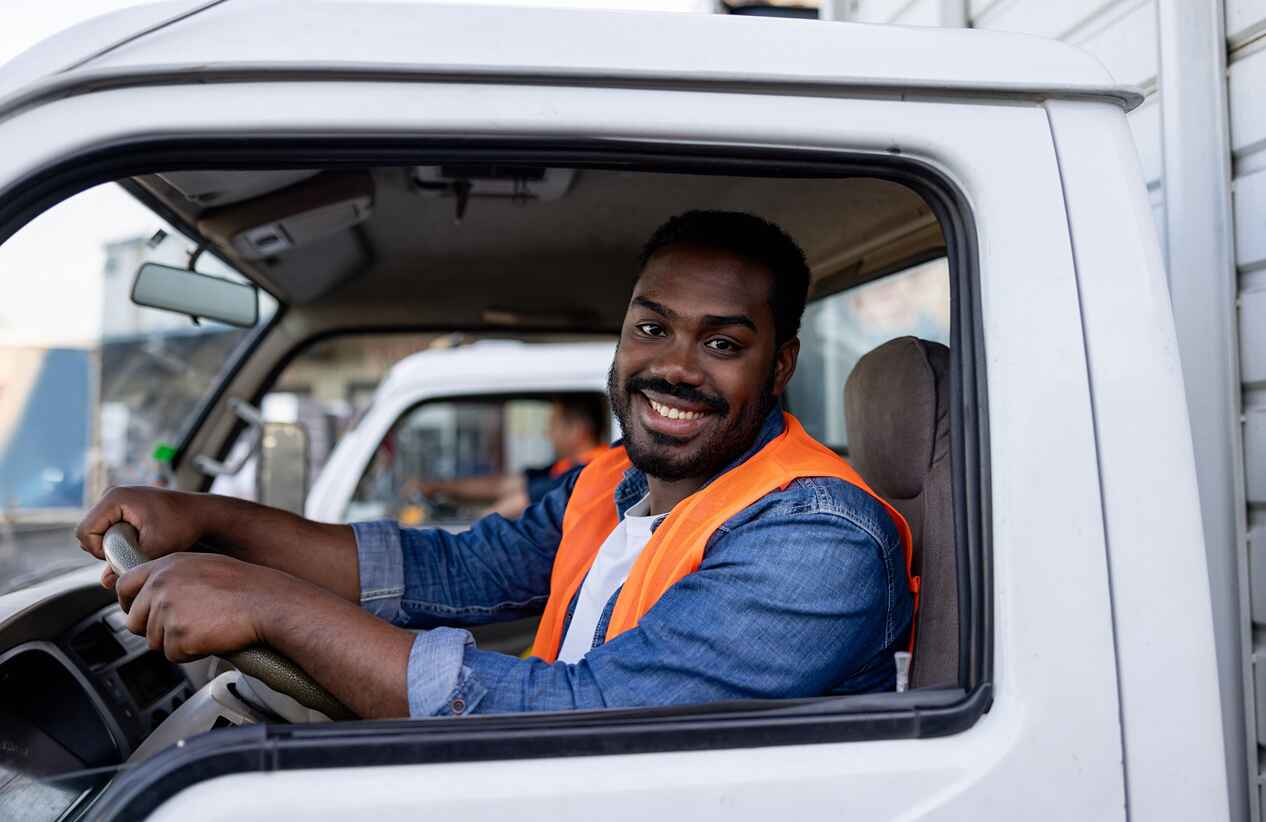 Portrait of a happy African American truck driver smiling while looking at the camera through the window - freight transportation concepts