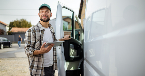 Young man looking at a tablet while standing next to a van with the door open