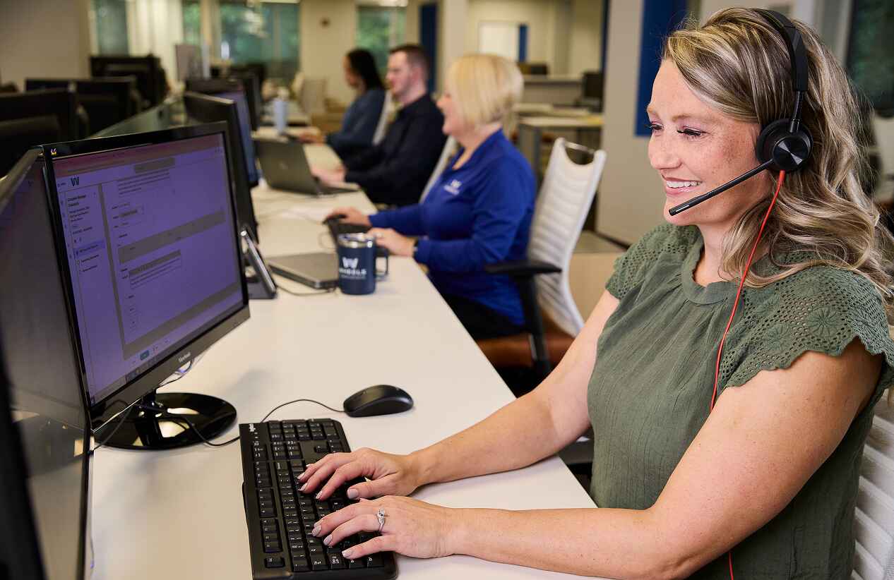 image of wheels employee working at a computer and smiling with a headset on