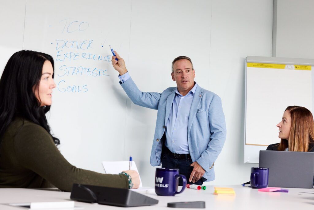 Wheels employees in a meeting; man writing on white board